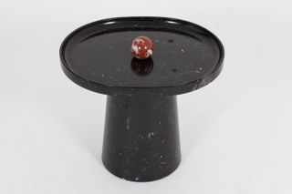 Red and white marble ball on a mushroom shaped black marble stand photographed against a grey background