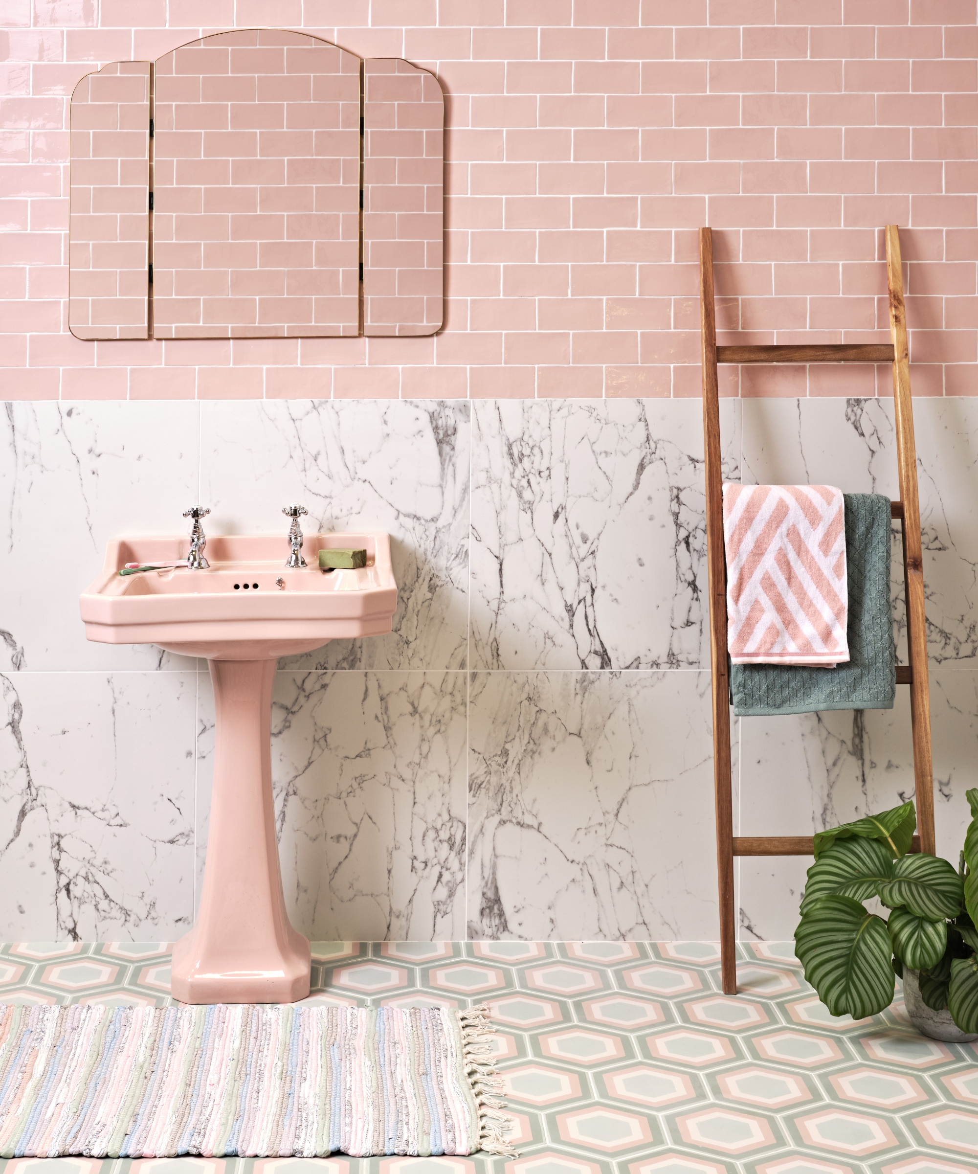 Pink pedestal sink against pink brick and marble tiles, wooden ladder with towels, hexagon tiled floor.