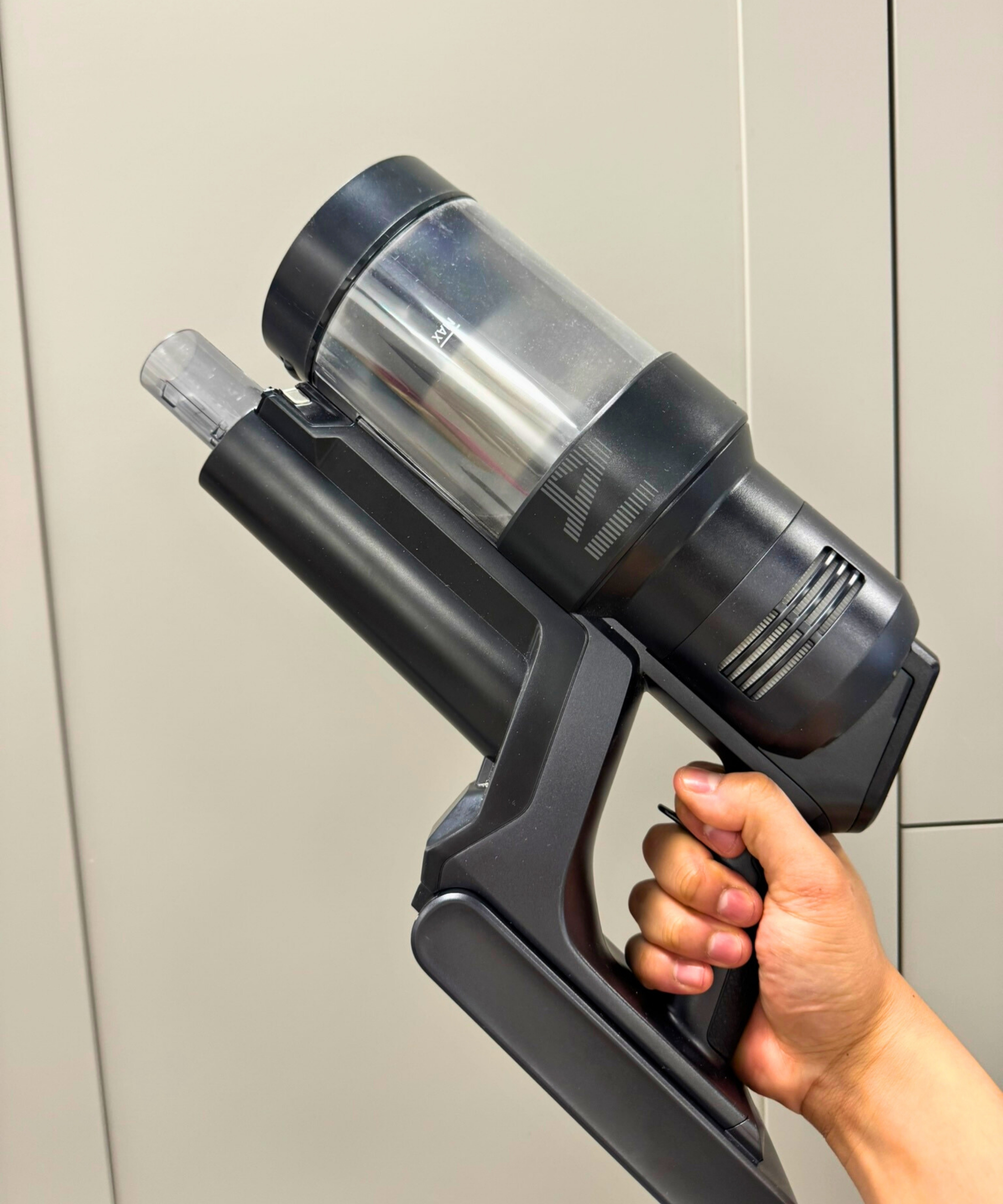 Hand holding the main vacuum unit of the Samsung Bespoke AI Jet Ultra in front of gray cabinets.