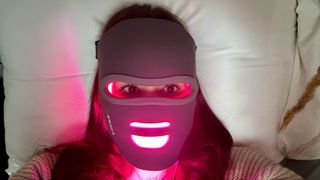 A girl wearing an LED face mask with pink light