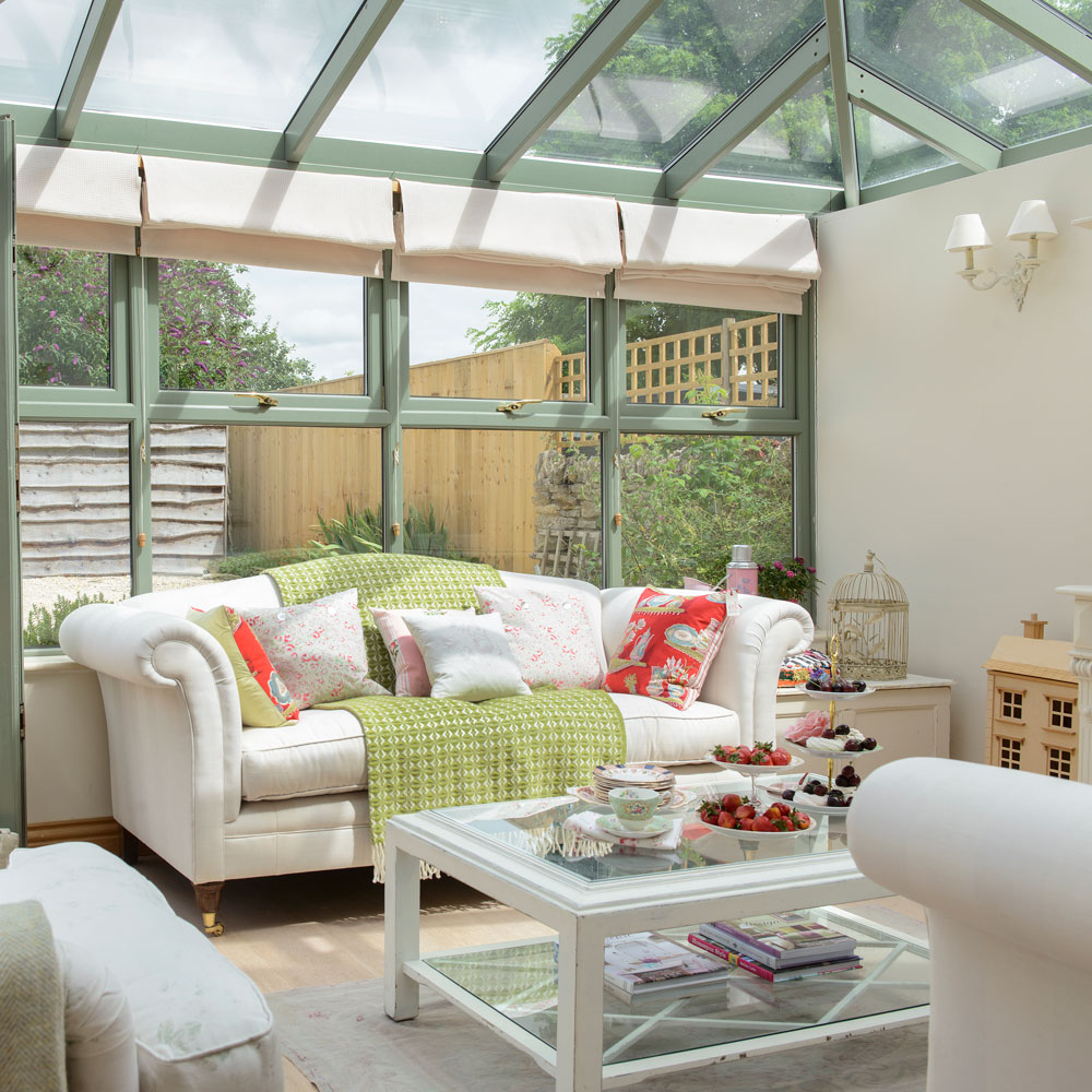 A green conservatory with cream furniture and a green throw