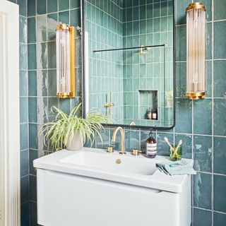 Green tiled bathroom with white wall hung vanity unity and reeded wall lights beside a mirror