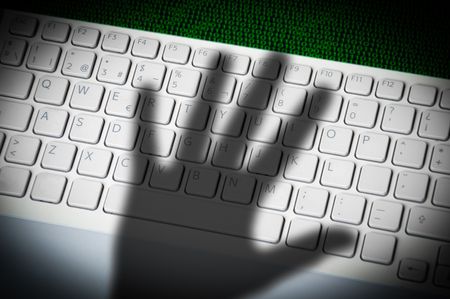 A menacing hand shadow on a computer keyboard in front of printed computer data.