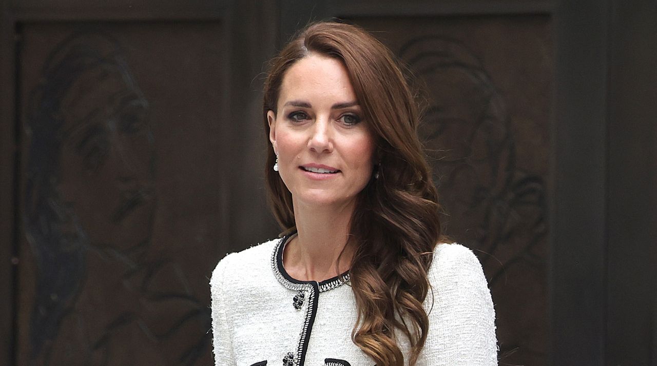 Kate Middleton has long brown hair and is wearing a white tweed jacket with black detailing