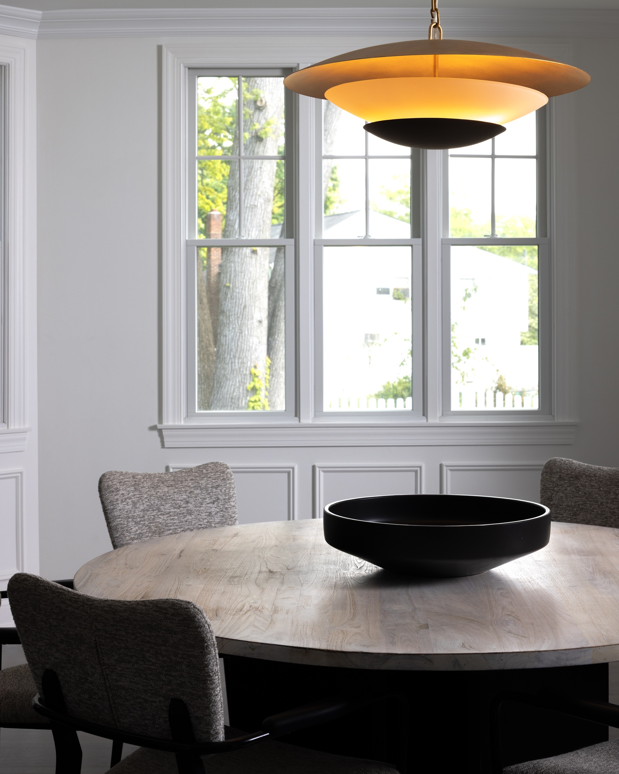a dining room with a round wooden table in front of a window and paneled wall