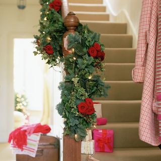 Brown carpeted stairs with wrapped gifts on stairs and fresh flower and foliage garland decorating the balustrade