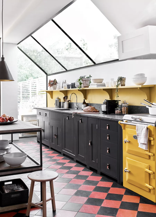 A black kitchen with yellow walls and yellow range cooker with black and terracotta red checkered floor