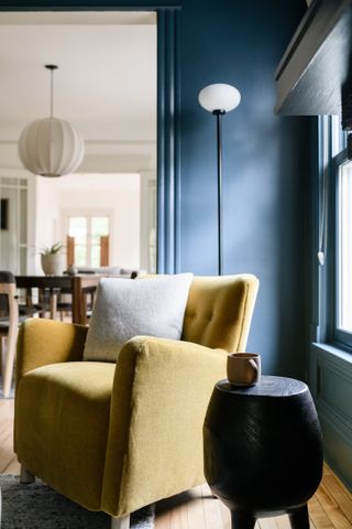 A living room in navy blue with a mustard yellow chair