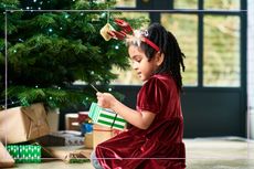 A young girl looking at a wrapped Chritsmas present under a Christmas tree