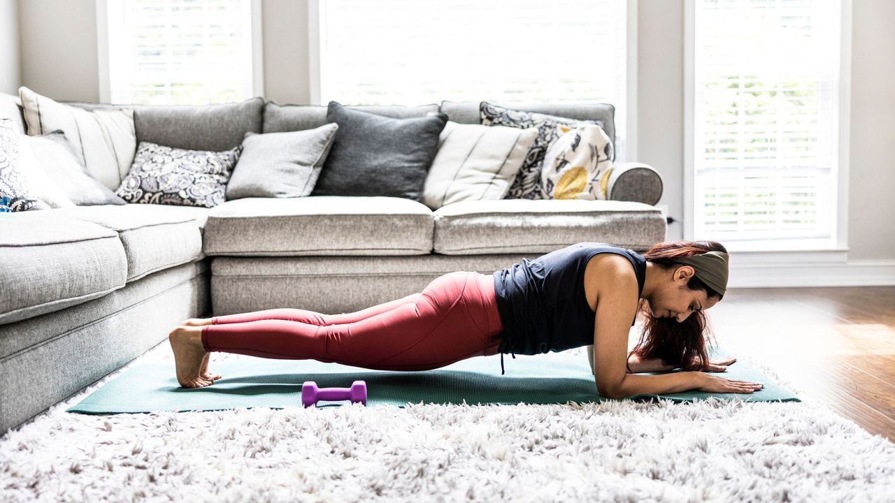 A woman performing a plank next to a set of dumbbells