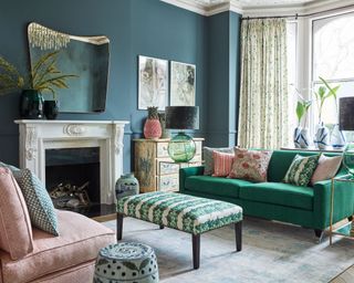 Living room with green sofa and assorted cushions and leaf pattern upholstered padded coffee table and sash window with light cushions and teal blue walls