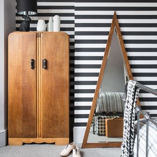 bedroom with black and white vertical stripe wallpaper with wooden wardrobe and triangular mirror