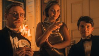 Two men and a woman look across a dimly lit table 