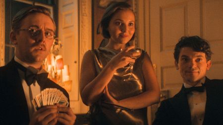 Two men and a woman look across a dimly lit table 