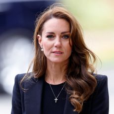Princess Kate Middleton wears a black blazer and black top and has long wavy brunette hair featuring blonde highlights