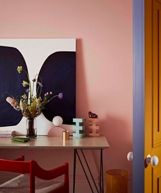 Home office with flamingo pink wall, red chair and abstract artwork
