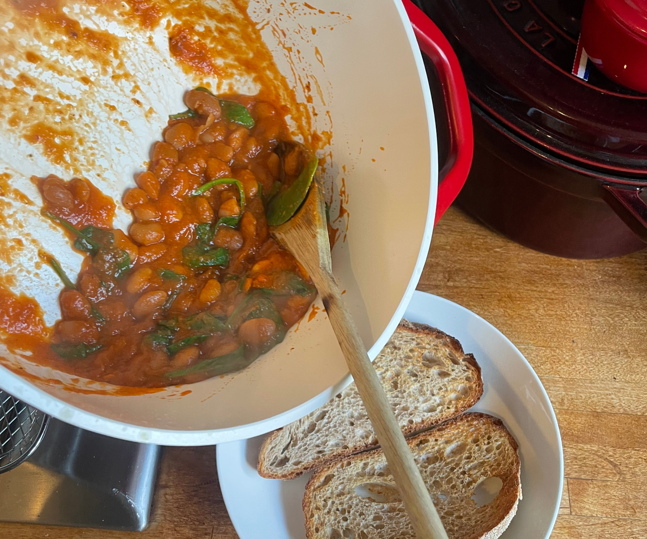 Pouring a bean mix from a pot onto two slices of toast on a white plate.
