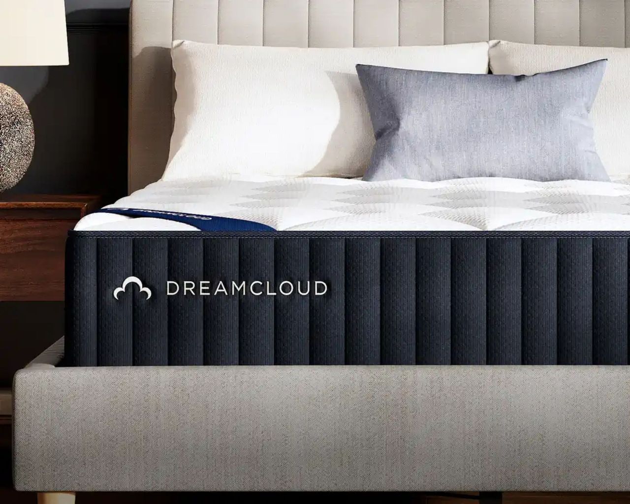 DreamCloud Hybrid Mattress on a grey bedframe with white cushions.