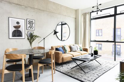 small apartment with brown leather sofa, round dining table and grey walls and area rug