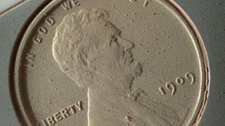 A close-up of the heads side of a penny covered in Mars dust. 
