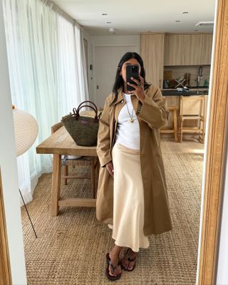 Monikh wearing a white tee, cream slip skirt, and a classic Burberry trench coat.