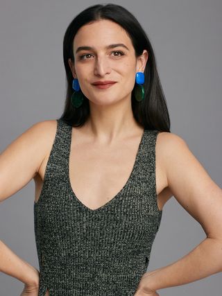 Jenny Slate posing for a photo in a sleeveless green knit dress and blue earrings