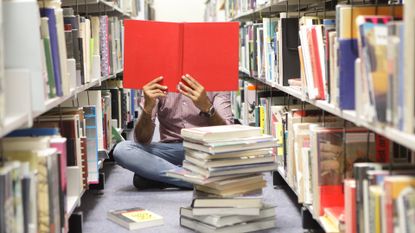 Person sat on floor in library reading red book