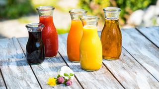 Lots of different juices in small containers on a wooden table with some flowers in front