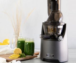 The Kuvings juicer in gray on a countertop with two jars of green juice to the left