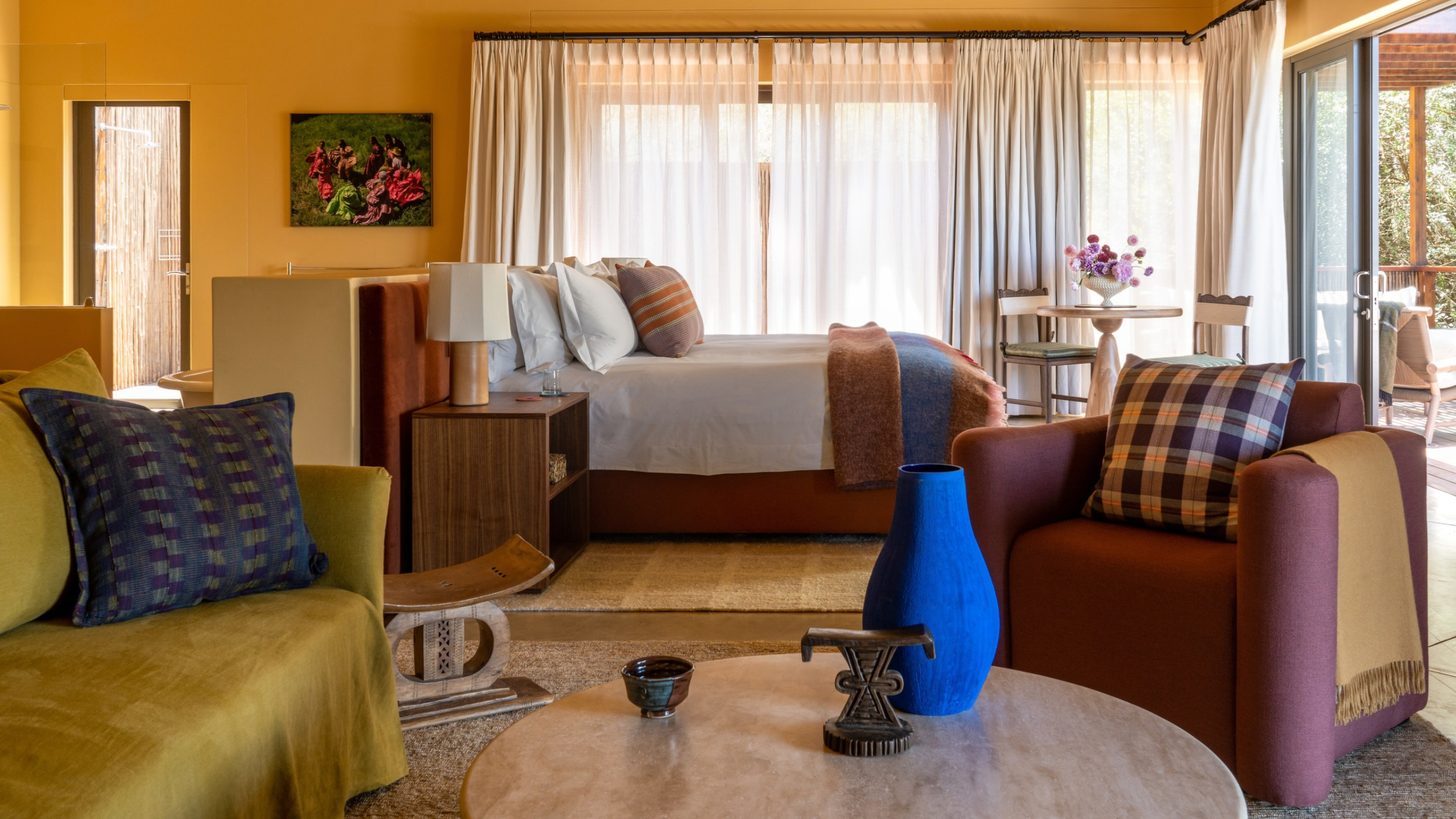 A room at the Tamodi Estate &amp; Polo Reserve in South Africa. Pictured is a yellow room with an olive couch, a plum armchair, a blue vase, and ceramic around a floating bed