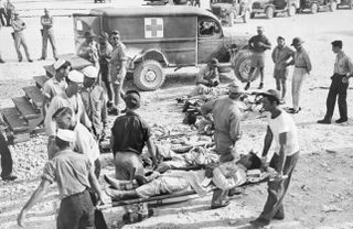 black and white scene with survivors of the USS Indianapolis on stretchers with an ambulance in the background