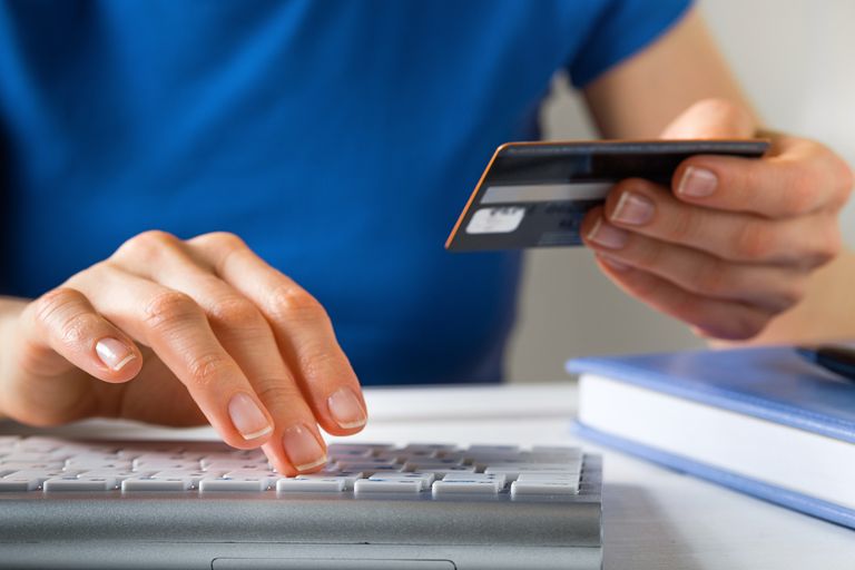 woman holding up a credit card and typing details into keyboard