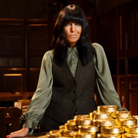 'The Traitors UK' host Claudia Winkleman stands in front of a stack on large gold coins.