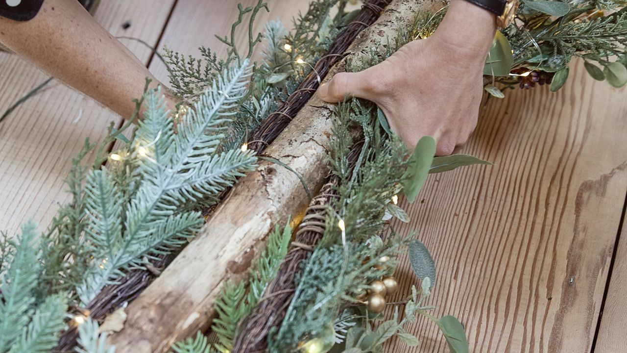 A space-saving wall Christmas tree being made by attaching foliage and string lights to a thick branch