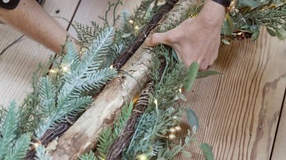 A space-saving wall Christmas tree being made by attaching foliage and string lights to a thick branch