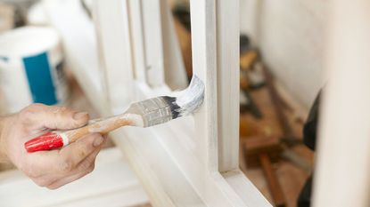 Someone using a paint brush to paint window trims white