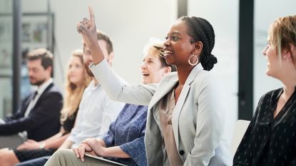 An employee raises her hand during an office meeting.