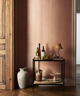 A bar cart against a pink wall on herringbone floorboards