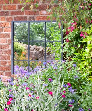 metal garden mirror against a red brick wall with pretty planting in front of it