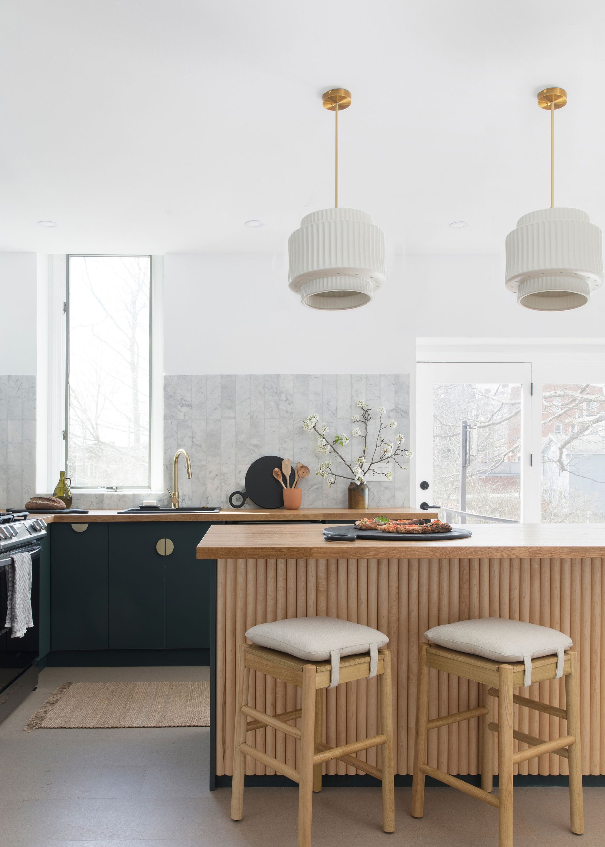 A panelled kitchen island with bar stools and hanging lamp shades above the kitchen island. On the left side are dark kitchen cabinets, adding a lovely contrast between the wooden and colorful cabinet.