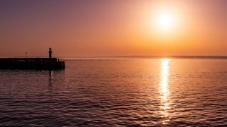 Fiery sunrise over the sea, with a pier to the left of the frame