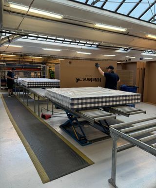 A Hästens mattress wrapped in plastic on a conveyor belt; a man carrying a cardboard box.