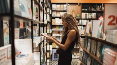 A woman with long brownish hair looks at a book inside a cozy bookstore
