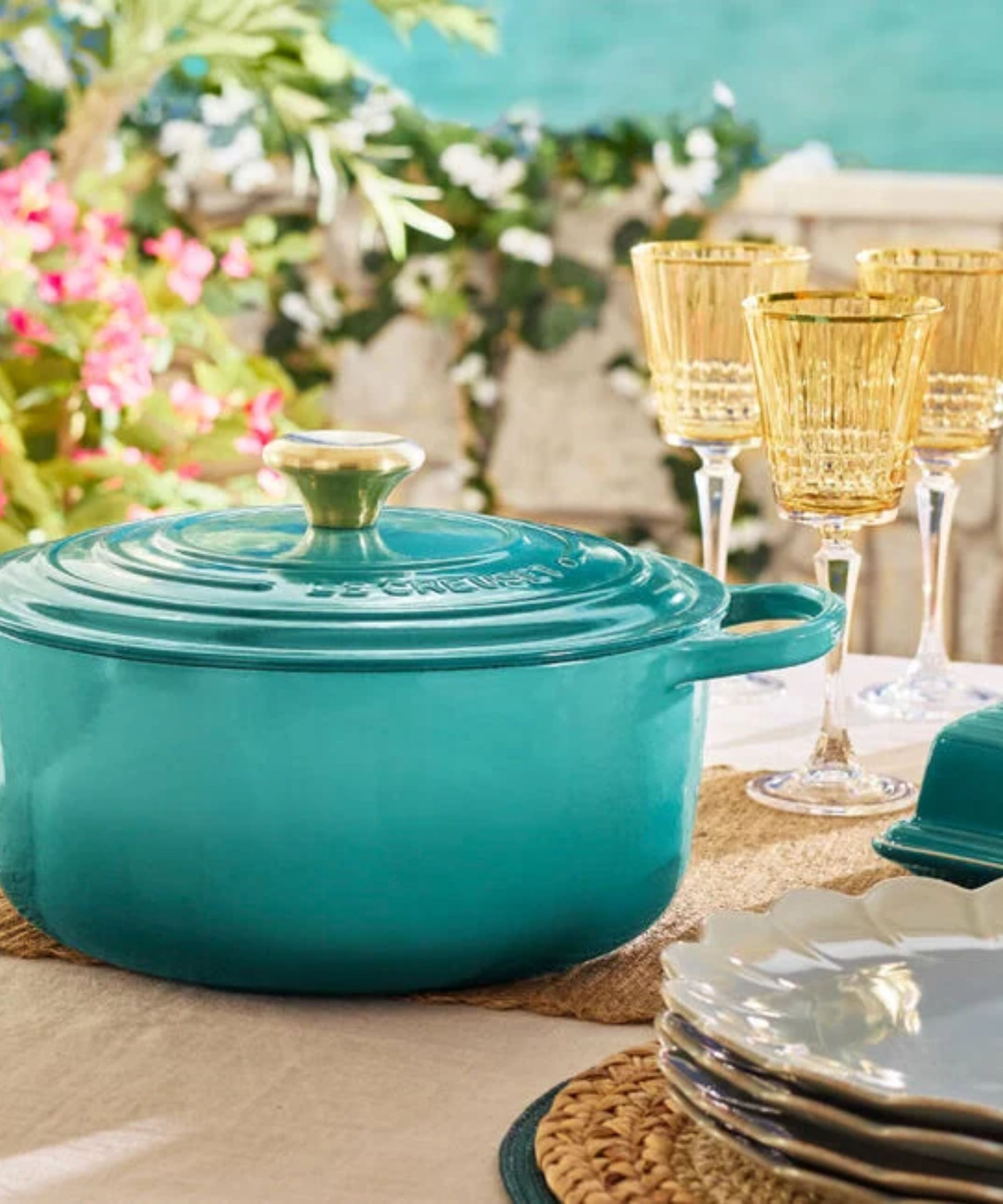 A blue Le Creuset Dutch Oven on an outdoor summer table surrounded by drinking glasses.