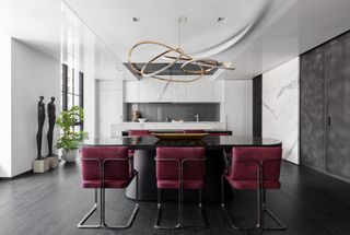 A kitchen with white walls, white marble cabinets and deep maroon chairs