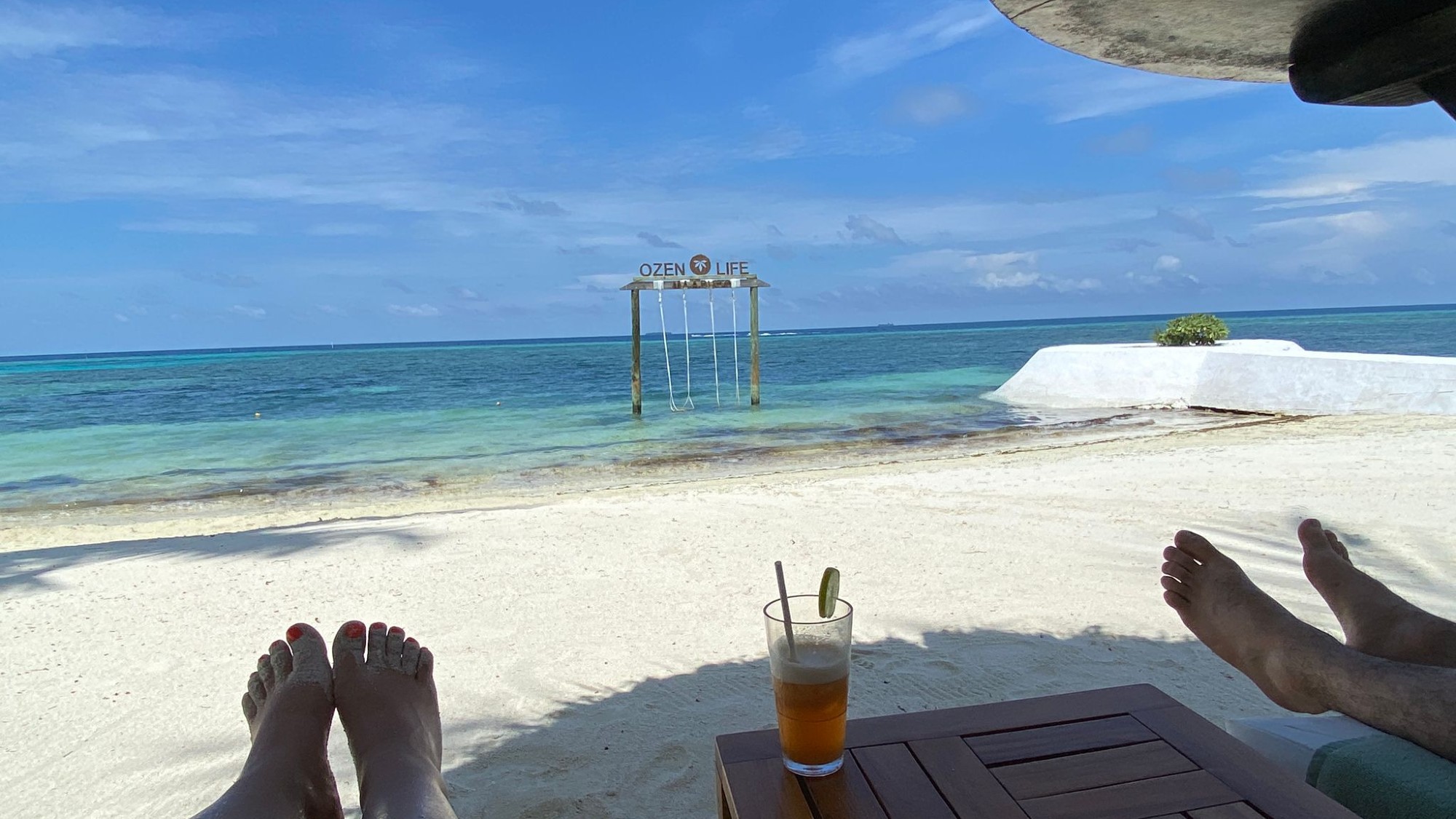 Shot of beach at OZEN Life Maadhoo, with swing and two pairs of feet in forefront