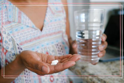 Woman holding two paracetamol tablets and a glass of water