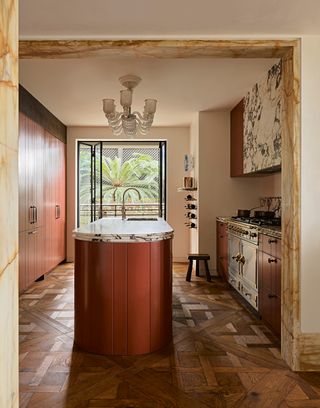 a small luxury kitchen with a red island and wood parquet flooring