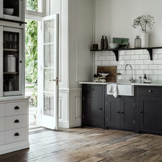 A monochromatic kitchen with wooden flooring, black cabinetry and shelves and white tallboy dresser