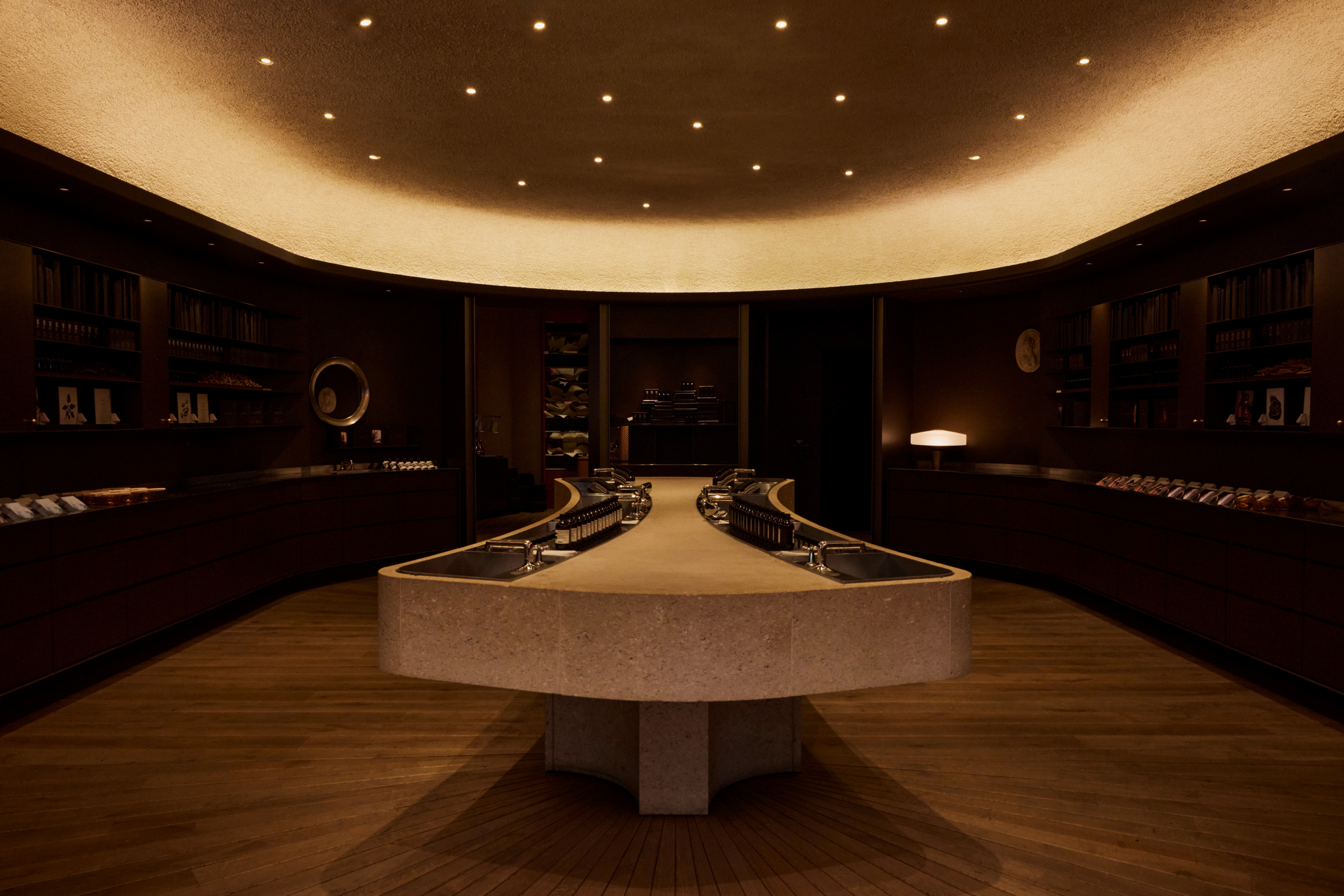 Interiors of a dimly lit, futuristically designed fragrance store with an illuminated roof, chocolatey interiors, and plenty of books and paper installations styled sophisitcatedly.